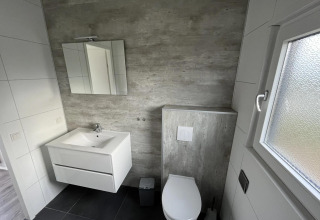 Baño moderno con inodoro suspendido, lavabo, espejo y ventana en Velthorst, Poort van Zeeland.
