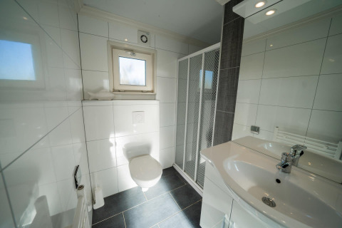 Baño moderno con inodoro suspendido, ducha, lavabo y ventana en lodge Velthorst, Poort van Zeeland.