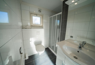 Baño moderno con inodoro suspendido, ducha, lavabo y ventana en lodge Velthorst, Poort van Zeeland.