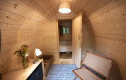 Acogedor interior de madera del Duo Pod en RØSTIG, Países Bajos, con banco y flores en la mesa.