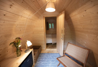 Acogedor interior de madera del Duo Pod en RØSTIG, Países Bajos, con banco y flores en la mesa.