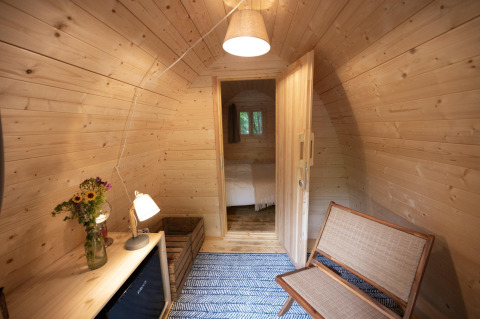 Acogedor interior de madera del Duo Pod en RØSTIG, Países Bajos, con banco y flores en la mesa.