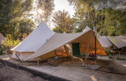 Vista del tent Solo Tipi en RØSTIG, Países Bajos, rodeado de árboles y luz solar de fondo.