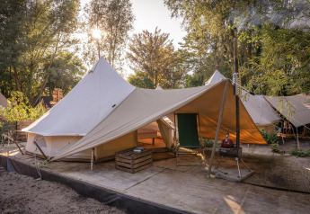 Vista del tent Solo Tipi en RØSTIG, Países Bajos, rodeado de árboles y luz solar de fondo.
