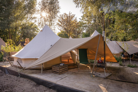 Vista del tent Solo Tipi en RØSTIG, Países Bajos, rodeado de árboles y luz solar de fondo.