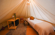 Interior de la tienda Solo Tipi en RØSTIG, Países Bajos, con cama individual y decoración acogedora.