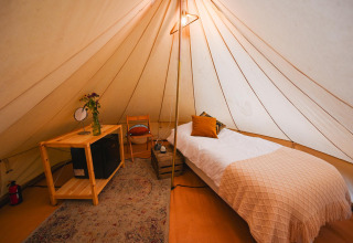 Interior de la tienda Solo Tipi en RØSTIG, Países Bajos, con cama individual y decoración acogedora.