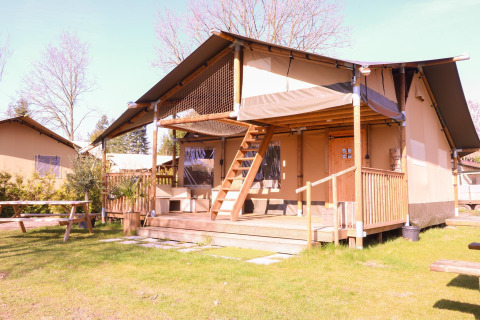 Tenda safari Ranger al Camping Vossenberg nei Paesi Bassi con veranda in legno e tavoli da picnic.