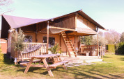 Tienda safari Ranger en Camping Vossenberg, Países Bajos, con terraza de madera y mesa de picnic exterior.