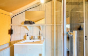 Badezimmer im Safari-Zelt Ranger auf Camping Vossenberg, Niederlande, mit Waschbecken, Spiegel und Dusche.