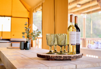 Vino y copas sobre bandeja de madera en Safari tent Ranger, Camping Vossenberg, Países Bajos, ambiente soleado.