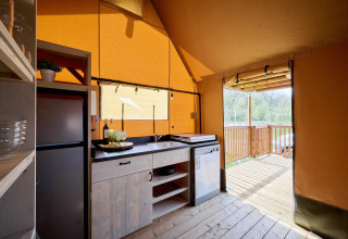 Vista interior de la tienda Safari Ranger en Camping Vossenberg, Países Bajos, con cocina y terraza exterior.