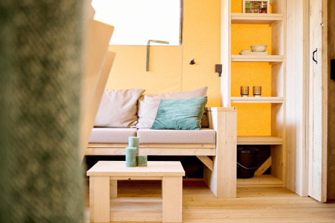 Cozy lounge in Safari tent Ranger at Camping Vossenberg, Netherlands, featuring sofa and wooden shelves.
