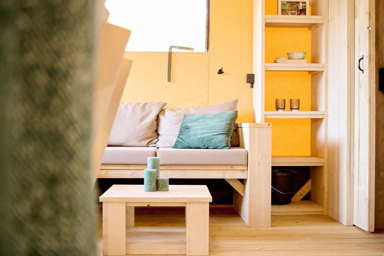 Acogedora sala en la tienda Safari Ranger de Camping Vossenberg, Países Bajos, con sofá y estantería.