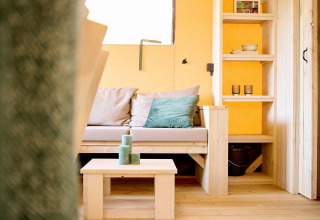 Cozy lounge in Safari tent Ranger at Camping Vossenberg, Netherlands, featuring sofa and wooden shelves.