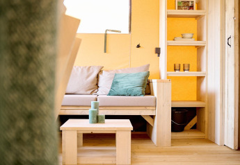 Cozy lounge in Safari tent Ranger at Camping Vossenberg, Netherlands, featuring sofa and wooden shelves.