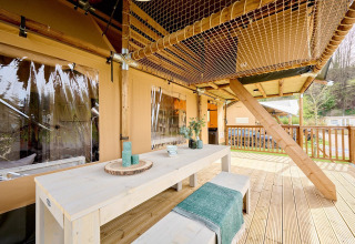 Terraza amplia con mesa de madera y techo de red en la Safari tent Ranger de Camping Vossenberg, Países Bajos.