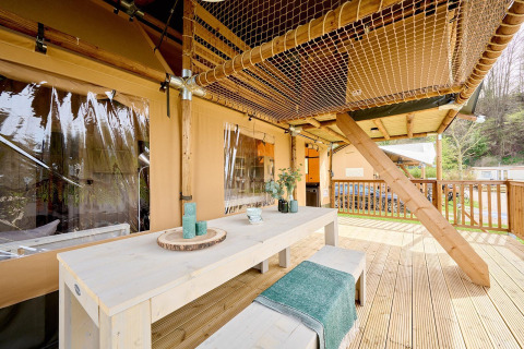 Houten terras met lange tafel en nettenplafond bij Safari tent Ranger op Camping Vossenberg, Nederland.