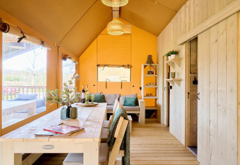 Interior de una espaciosa tienda safari en Camping Vossenberg, Países Bajos, con muebles de madera.
