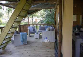 Terraza de madera con sofás y escalera en Safari tent Ranger en Camping Vossenberg, Países Bajos, rodeada de naturaleza.