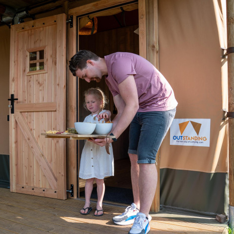Hombre y niña disfrutan de bocadillos frente a su tienda safari en Camping Vossenberg, Países Bajos.
