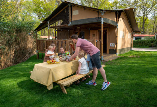Familia disfrutando de una comida al aire libre junto a la tienda Safari Ranger en Camping Vossenberg, Países Bajos.