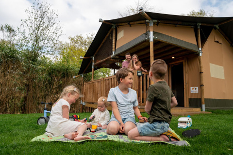 Kinder spielen auf dem Rasen vor einem Safarizelt auf dem Campingplatz Vossenberg in den Niederlanden.
