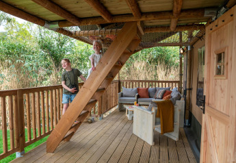 Dos niños juegan en las escaleras de la terraza de una tienda safari con muebles de madera en Camping Vossenberg, Países Bajos.
