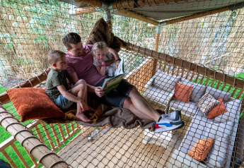 Familia leyendo juntos en una red dentro de la Safari tent Ranger en Camping Vossenberg, Países Bajos.
