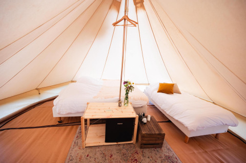 Interieur van een tipi met twee bedden, houten meubels en decoratie in Triple Tipi bij RØSTIG, Nederland.