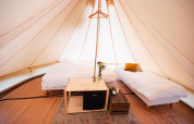 Indretning i en luksuriøs tipi med to senge, blomster, minikøleskab og træmøbler på RØSTIG, Holland.