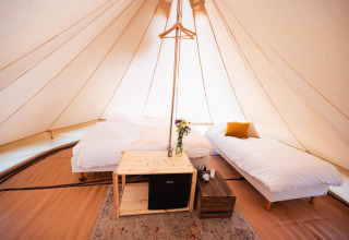 Indretning i en luksuriøs tipi med to senge, blomster, minikøleskab og træmøbler på RØSTIG, Holland.