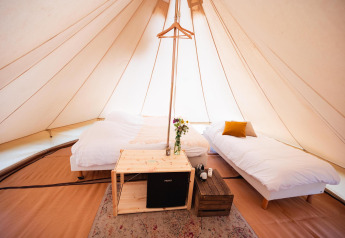 Innenraum eines geräumigen Tipis mit zwei Betten, Holztisch und Dekoration im Triple Tipi bei RØSTIG, Niederlande.