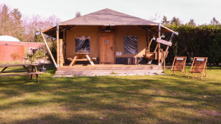 Safari tent Cottage at Camping Vossenberg in the Netherlands with deck chairs, picnic tables, and trees around.