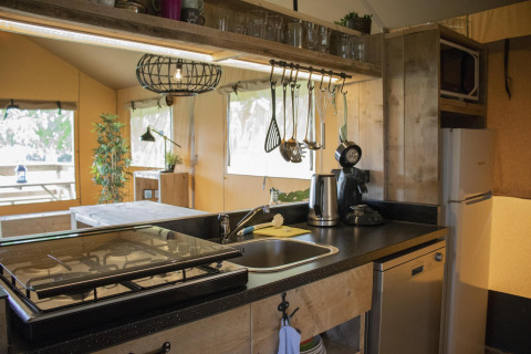 Área de cocina dentro de la Safari tent Cottage en Camping Vossenberg, con estufa, fregadero y nevera.