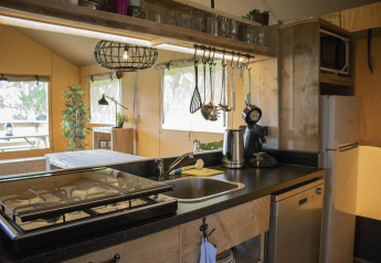 Área de cocina dentro de la Safari tent Cottage en Camping Vossenberg, con estufa, fregadero y nevera.