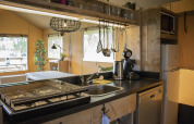 Kitchen area inside a Safari tent Cottage at Camping Vossenberg, featuring stove, sink, and fridge.