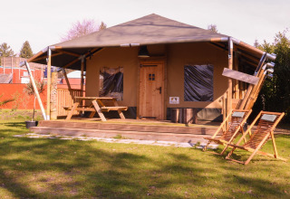 Tienda safari Cottage en Camping Vossenberg, Países Bajos, con terraza de madera y muebles de jardín.