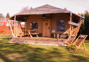 Tienda safari Cottage en Camping Vossenberg, Países Bajos, con terraza de madera y muebles de jardín.