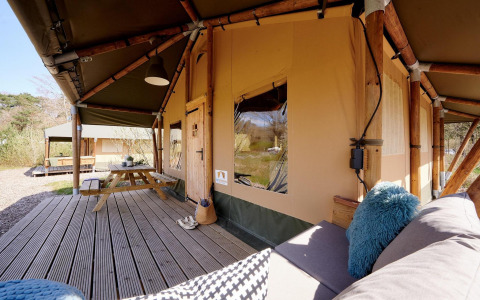 Tenda safari Cottage al Camping Vossenberg nei Paesi Bassi con terrazza in legno e sedute all’aperto.