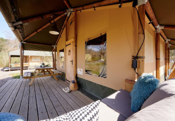 Tienda safari Cottage en Camping Vossenberg en Países Bajos, con terraza de madera y zona de estar.