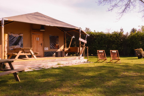 Safari telt Cottage ved Camping Vossenberg i Holland med træmøbler og en grøn græsplæne foran.