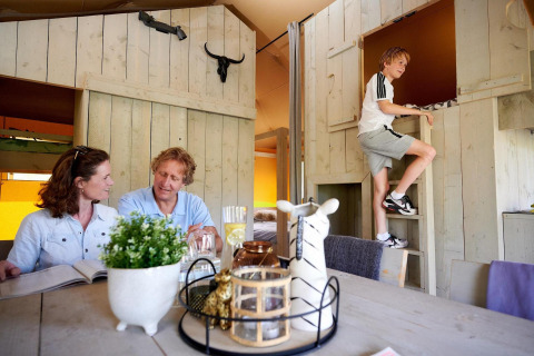 Familia disfruta en tienda safari en Camping Vossenberg, Países Bajos, niño sube escalera de madera.