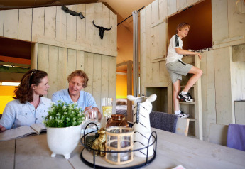 Family relaxing in Safari tent Cottage at Camping Vossenberg, Netherlands, boy climbs wooden ladder inside.