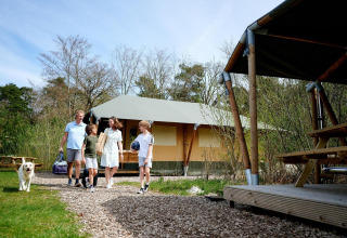 Familie med hund nyder sommerdag foran safari telt Cottage på Camping Vossenberg i Holland, omgivet af natur.
