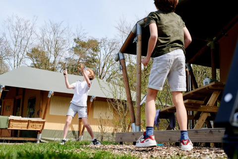 Dos niños juegan bádminton frente a una tienda safari en Camping Vossenberg, Países Bajos.