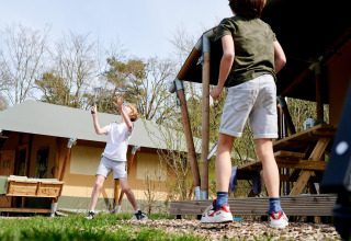 Dos niños juegan bádminton frente a una tienda safari en Camping Vossenberg, Países Bajos.