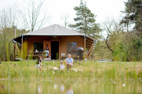 Familia disfruta de actividades al aire libre frente a la tienda Safari Cottage en Camping Vossenberg, Países Bajos.