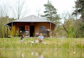 Familia disfruta de actividades al aire libre frente a la tienda Safari Cottage en Camping Vossenberg, Países Bajos.