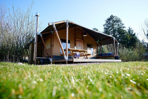 Tienda Safari Cottage en Camping Vossenberg, Países Bajos, con porche, mesa de picnic y césped verde.
